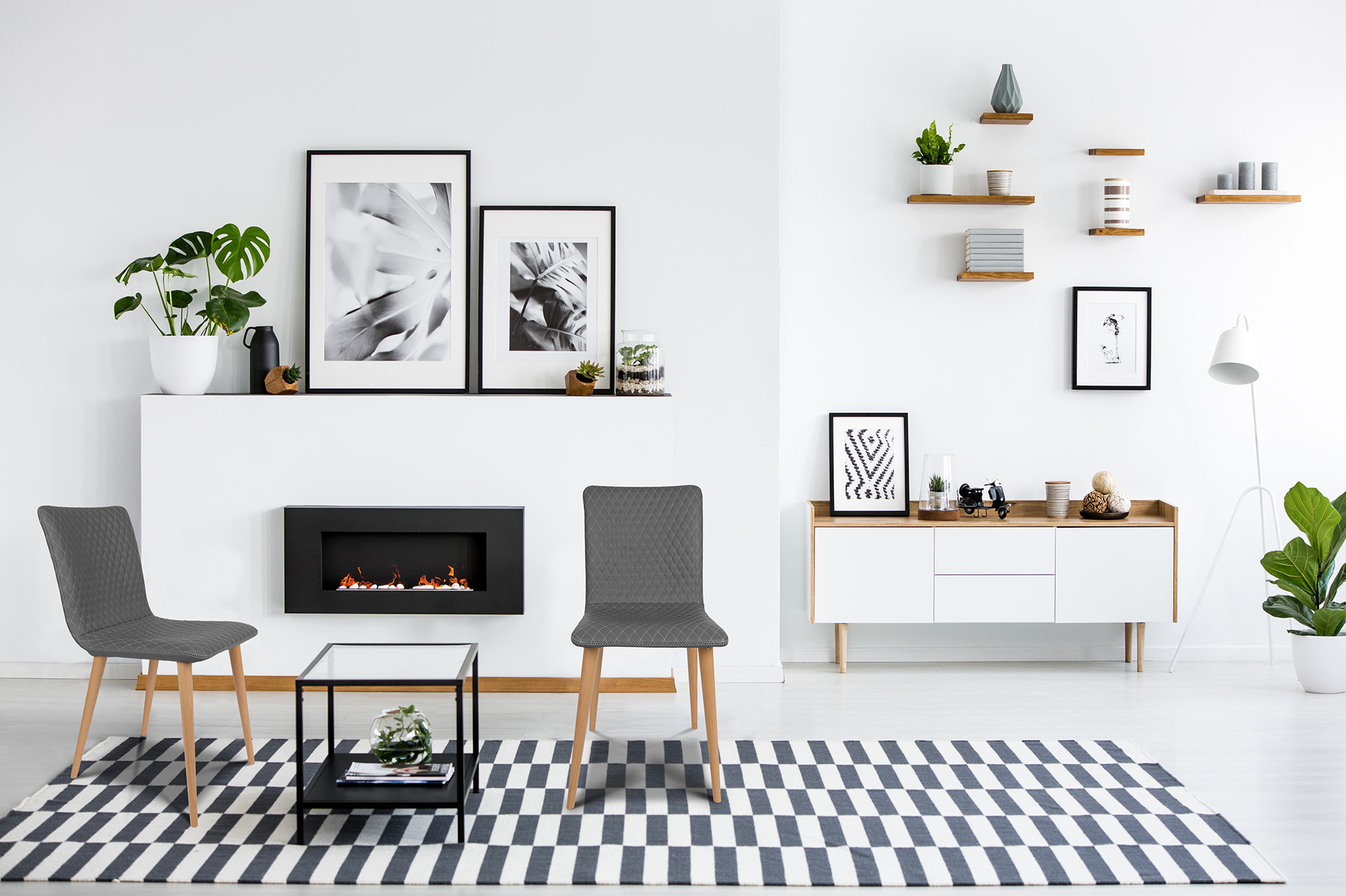 Fireplace between grey armchairs in modern living room interior with posters and plants. Real photo